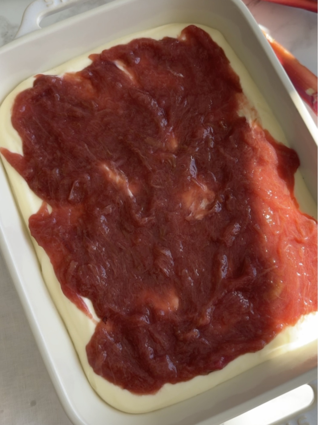 a layer of ladyfingers and mascarpone filling and rhubarb compote in a serving dish.